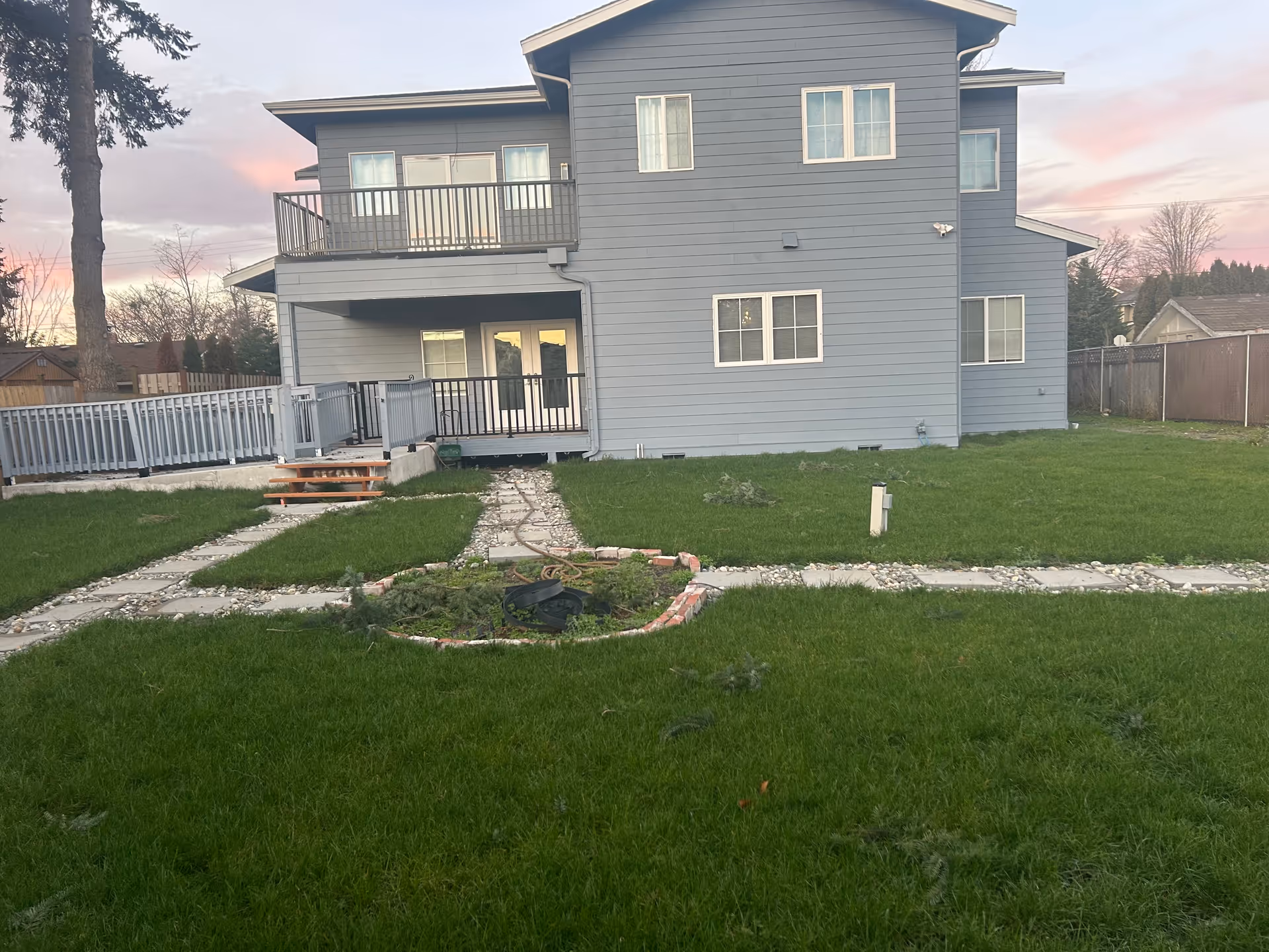 Blue two-story house with a raised deck, brick path, and green lawn.