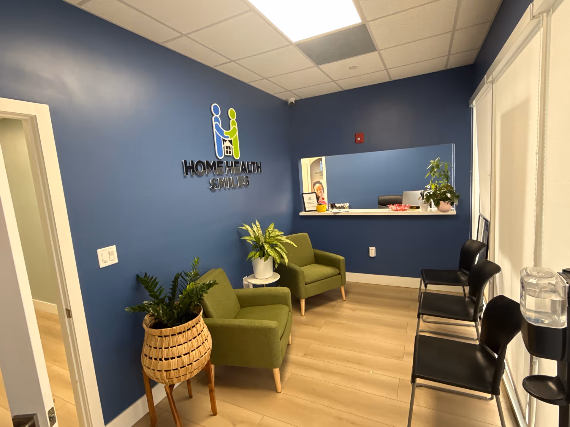 Blue-walled reception area with green chairs, plants, and a Home Health Smiles logo.