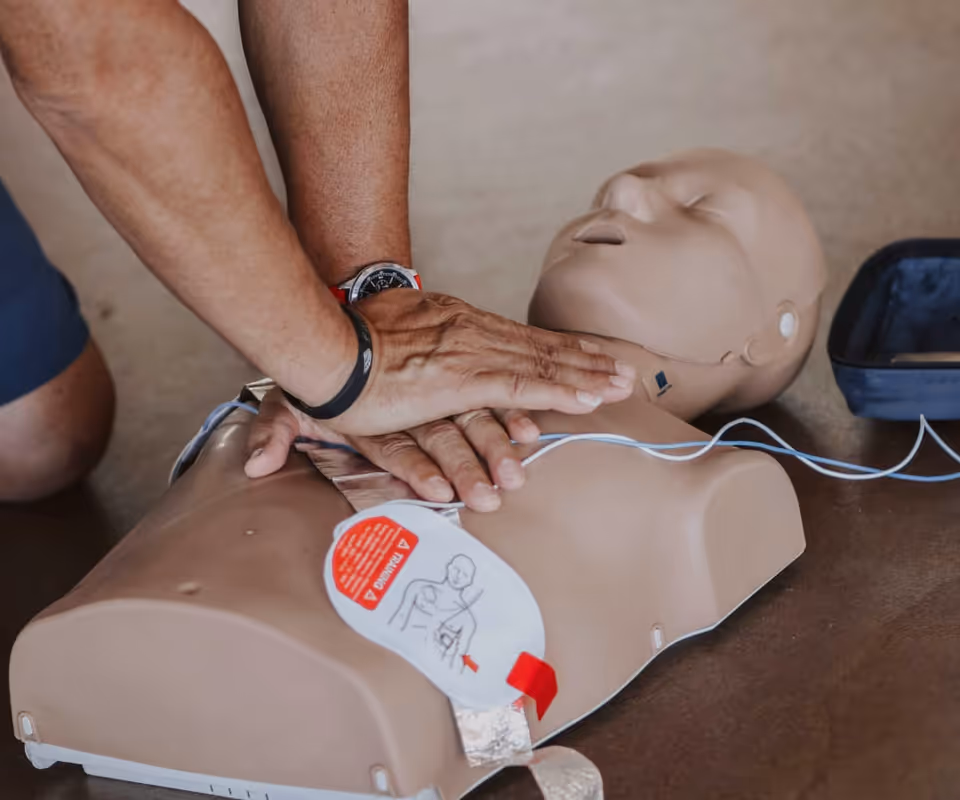 Hands perform chest compressions on a CPR training dummy on the floor.