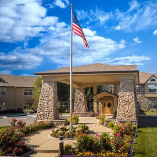 Atria Grass Valley senior living facility exterior with stone entrance pillars, American flag, and landscaped path.