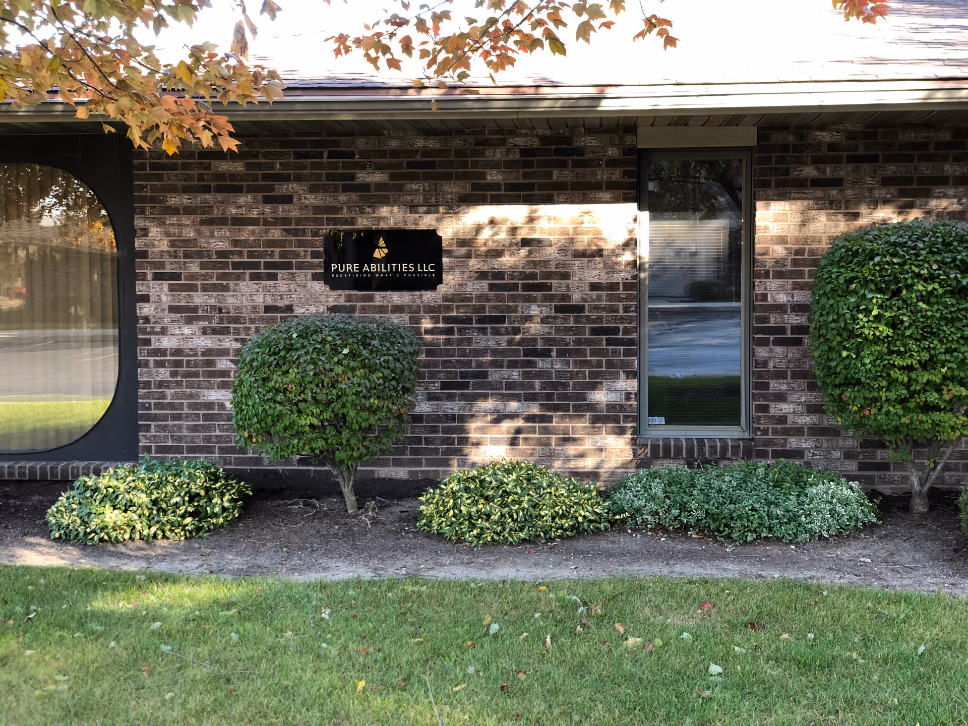 Brick building exterior with a Pure Abilities LLC sign and trimmed shrubs.