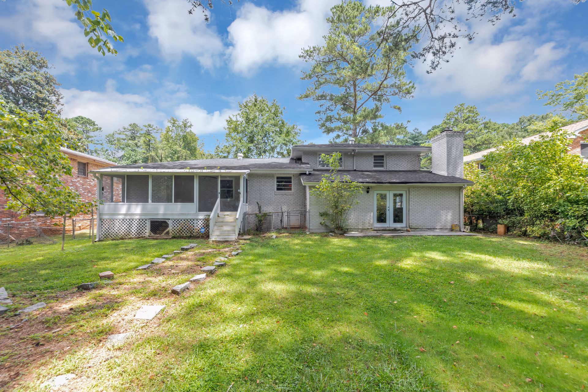 Backyard view of a single-story gray brick house with a green lawn.