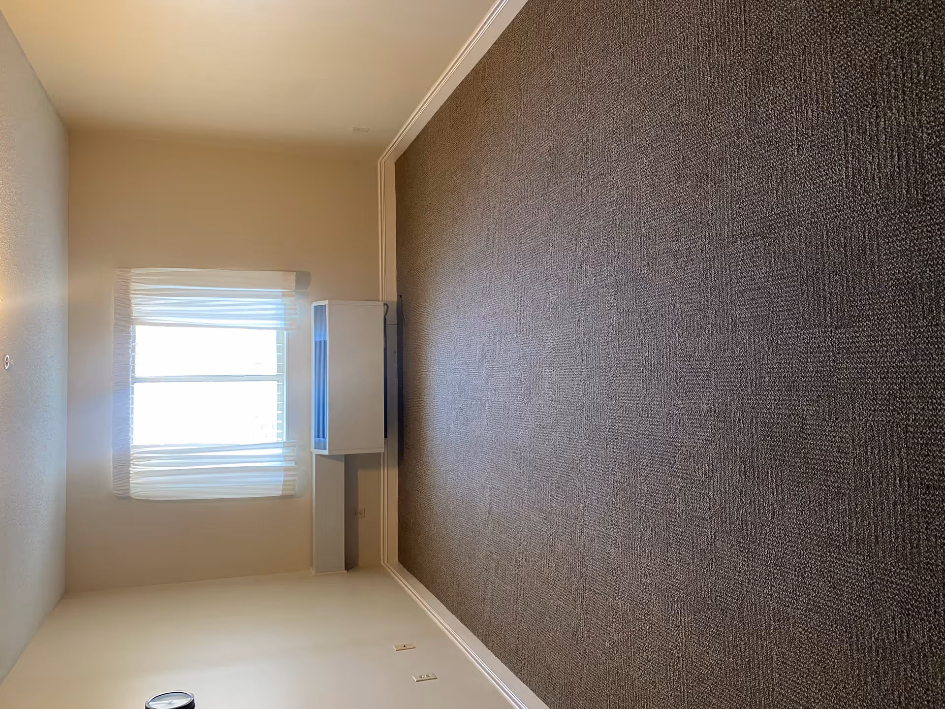 Bright beige room with a window, blinds, and a small white cabinet along the wall.