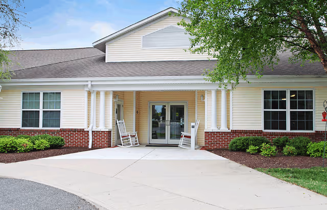 Front entrance of Seaton Chesterfield senior living with columns and rocking chairs.