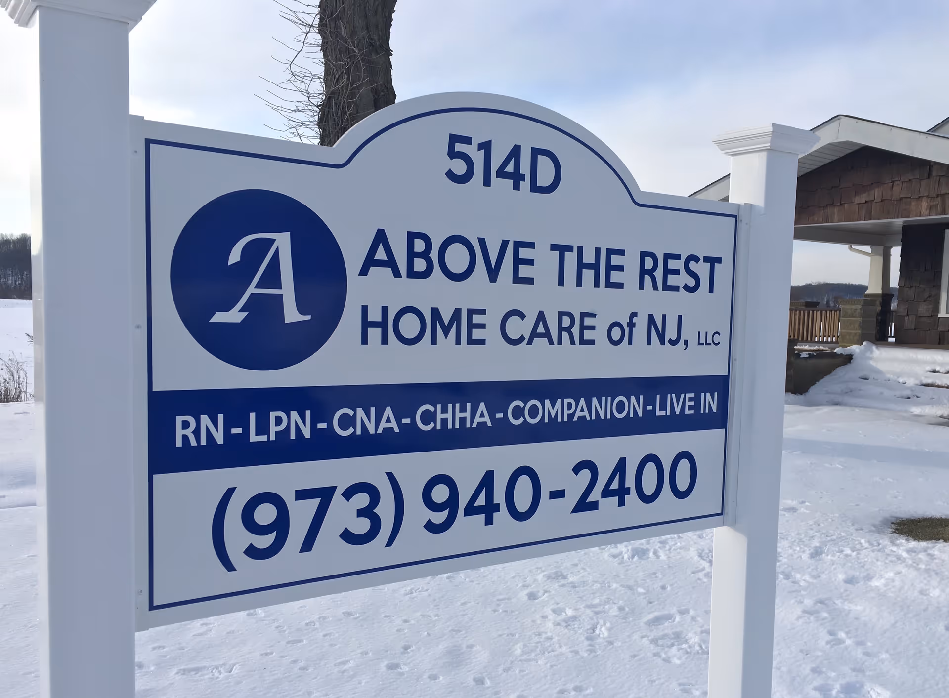 A large white and blue sign for Above the Rest Home Care of NJ, in snow.