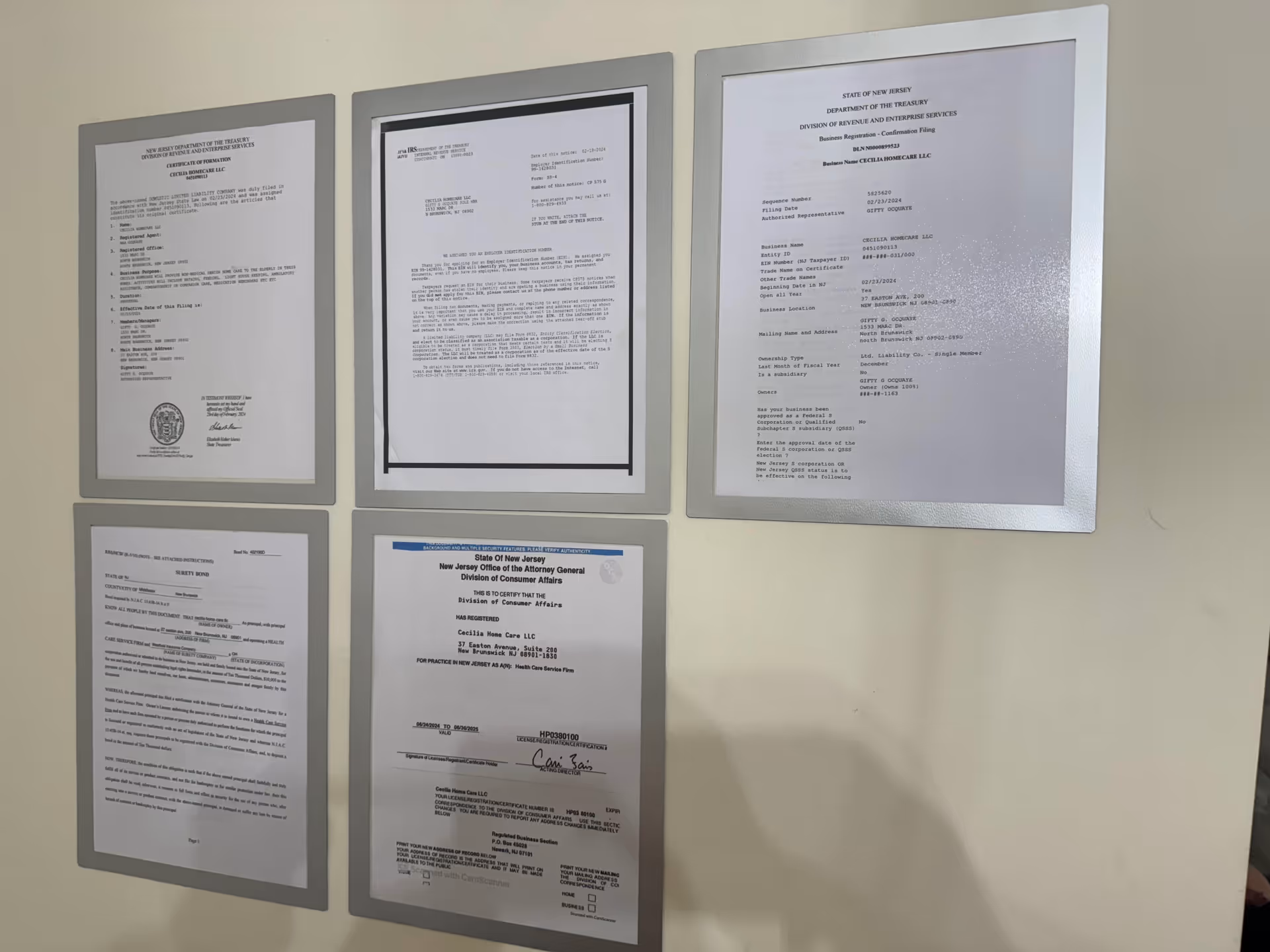 Six framed documents posted on a white wall inside a facility hallway