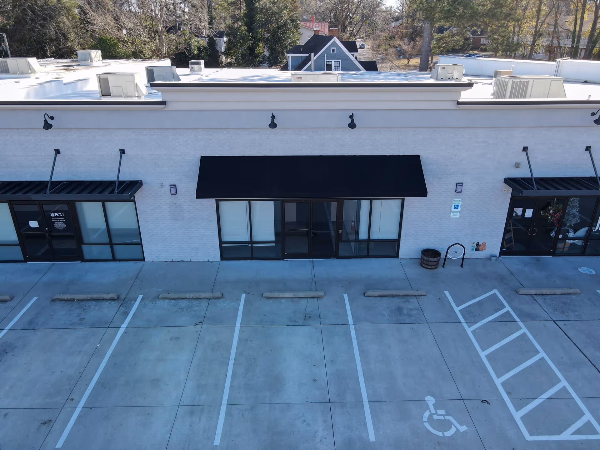Exterior of a white brick building with black awnings and adjacent parking spaces.
