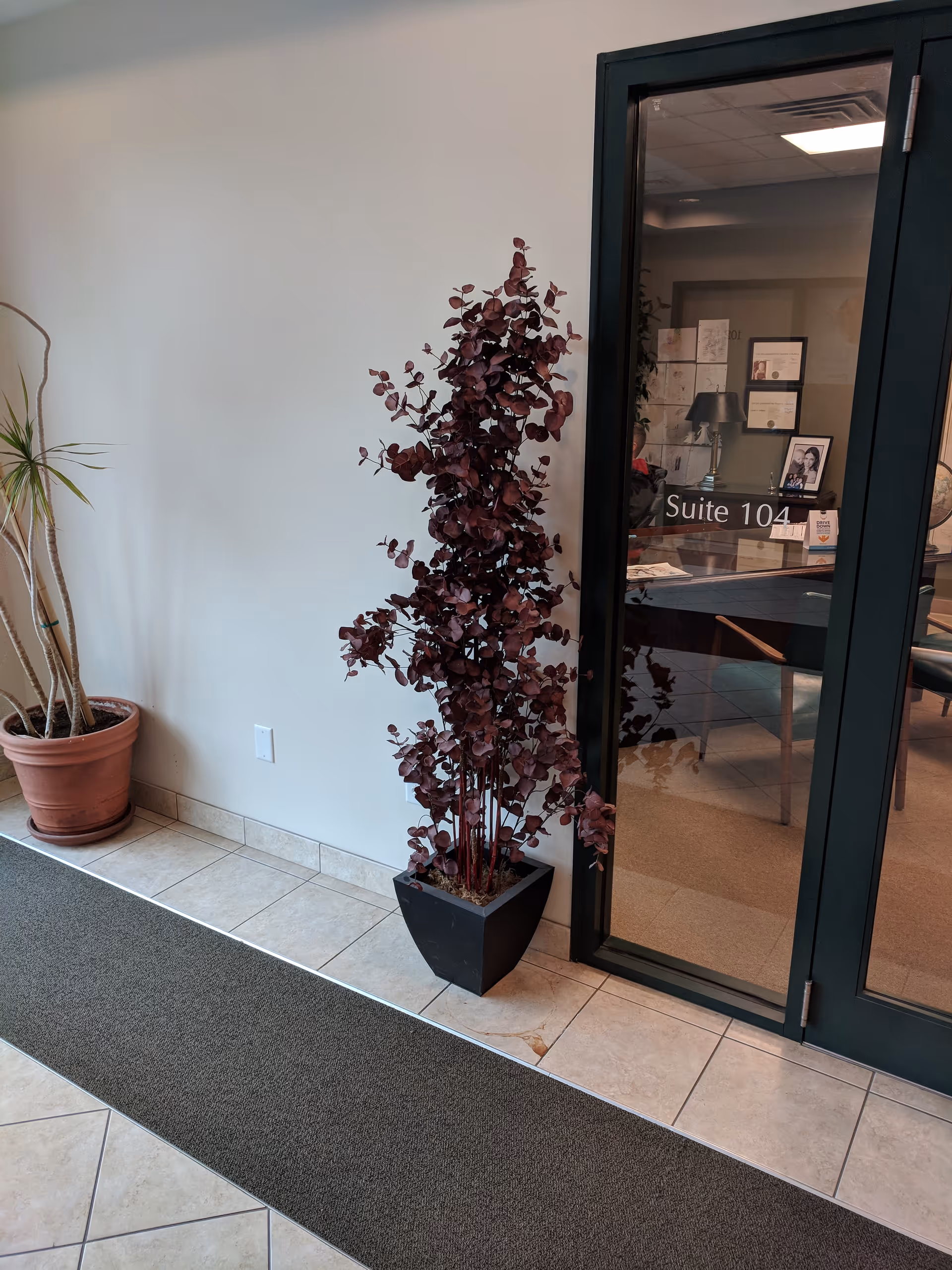Indoor lobby area with potted plant and glass door labeled Suite 104.