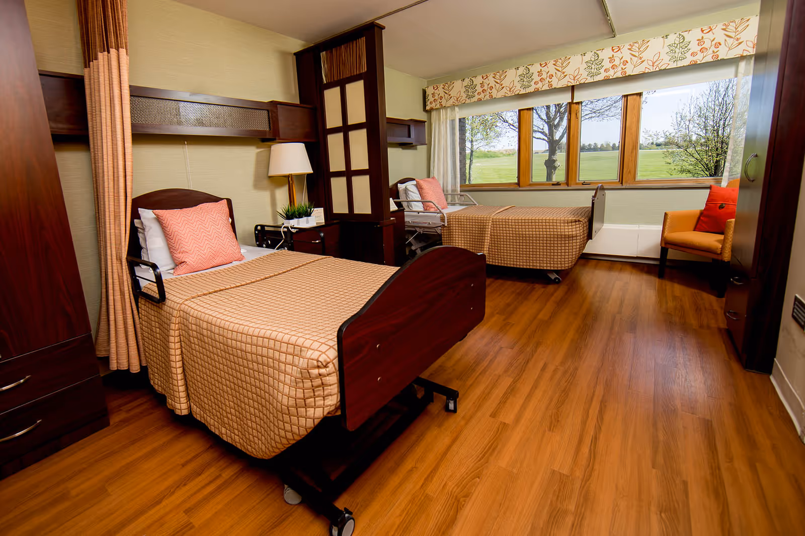 A spacious senior living bedroom with two adjustable beds, wood floors, and large windows.