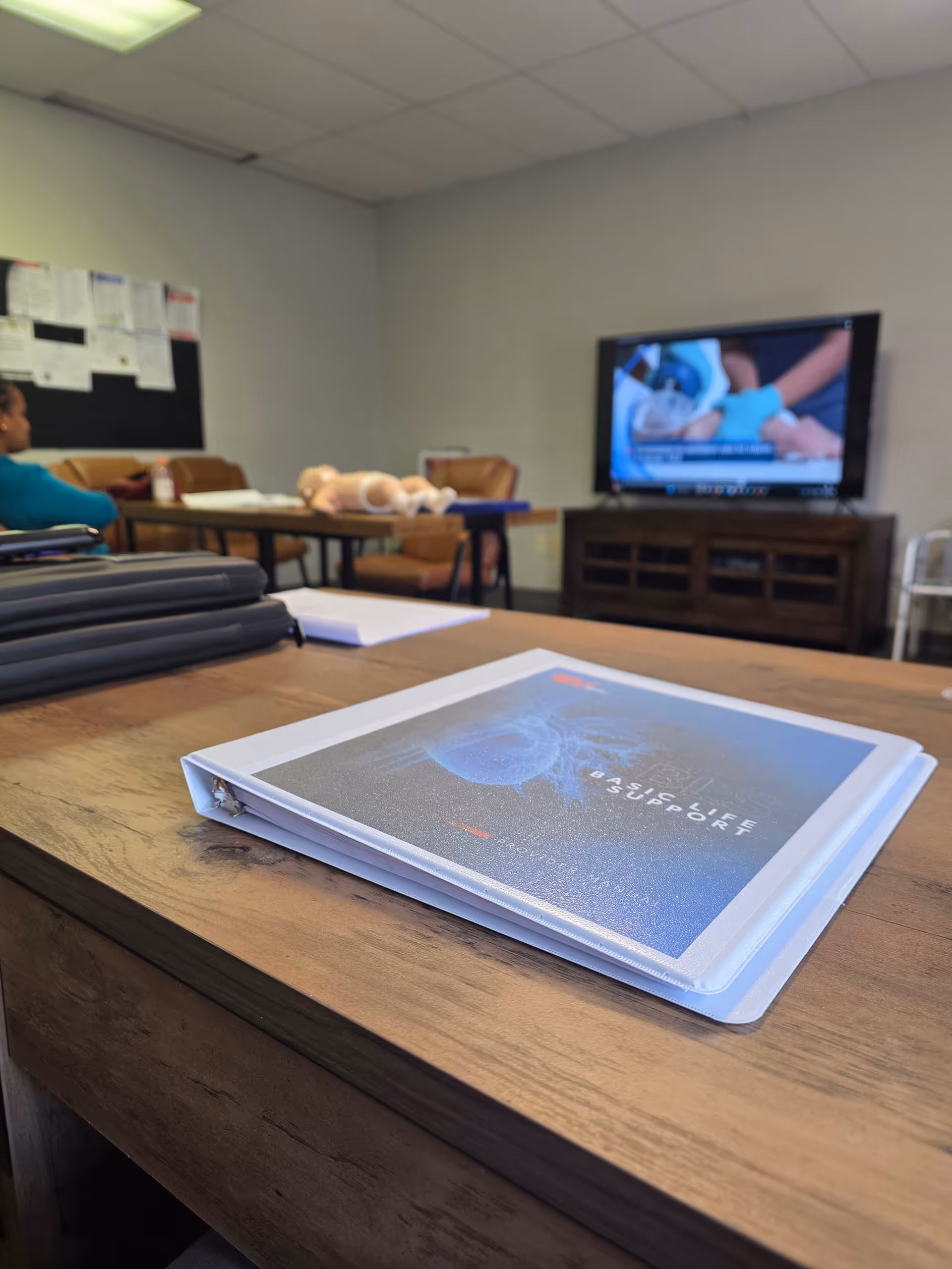 Elite Medical Training classroom with CPR manikins, a TV, and a binder on the table.