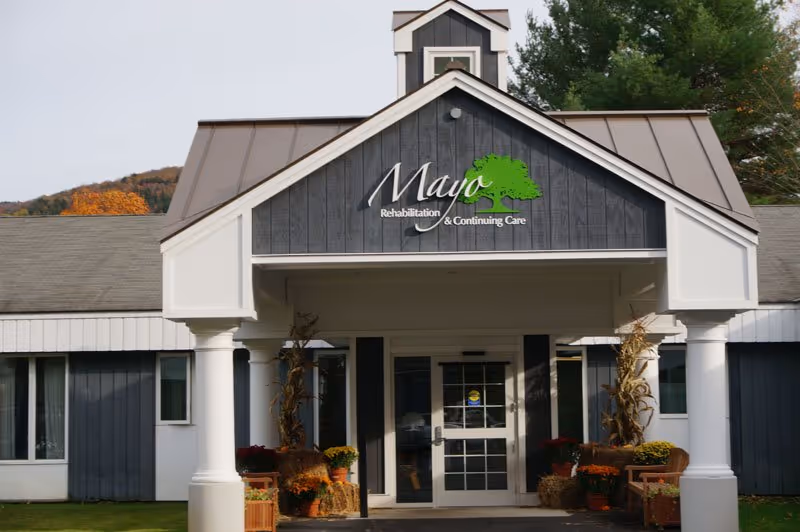 Front entrance of Mayo Healthcare facility with sign and autumn planters.