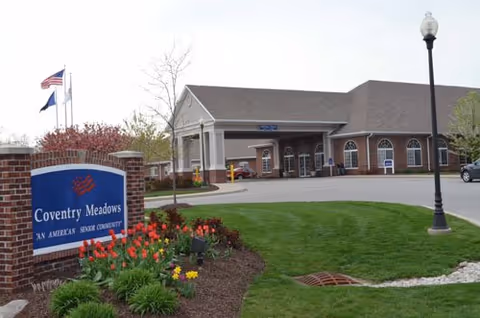 Exterior view of Coventry Meadows senior living facility with sign, entrance, and landscaped lawn.