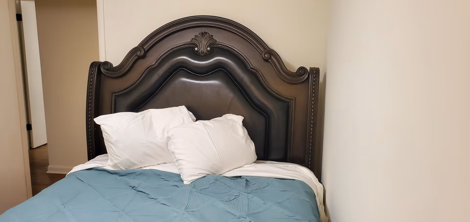 A dark ornate headboard bed with white pillows and blue blanket in a bedroom.