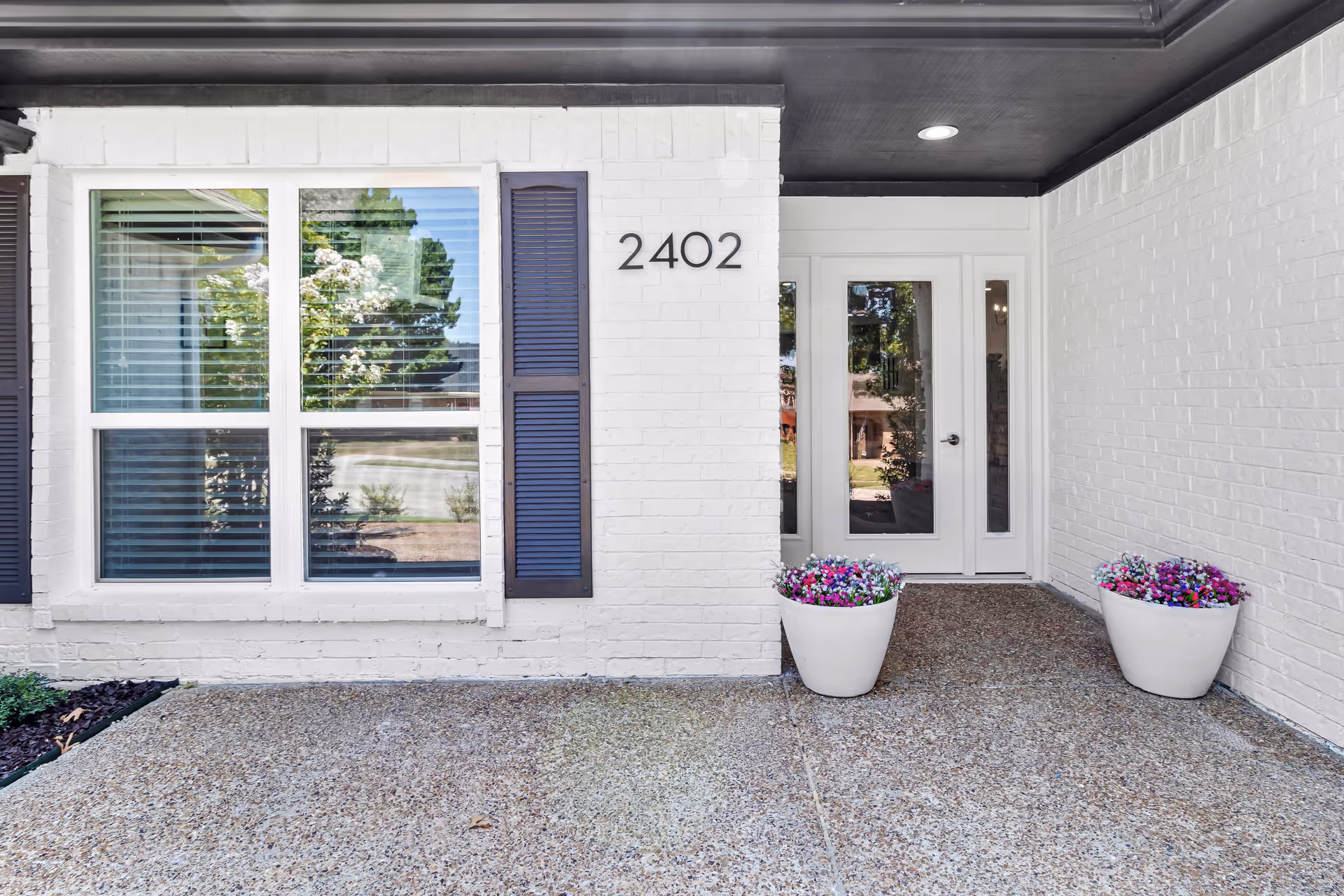 White brick building entrance with glass door, 2402, and two white planters with flowers