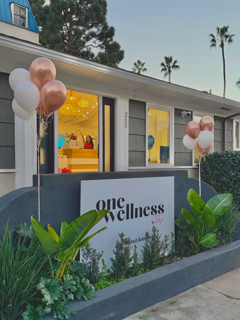 Front view of a wellness clinic storefront with balloons and a receptionist inside.