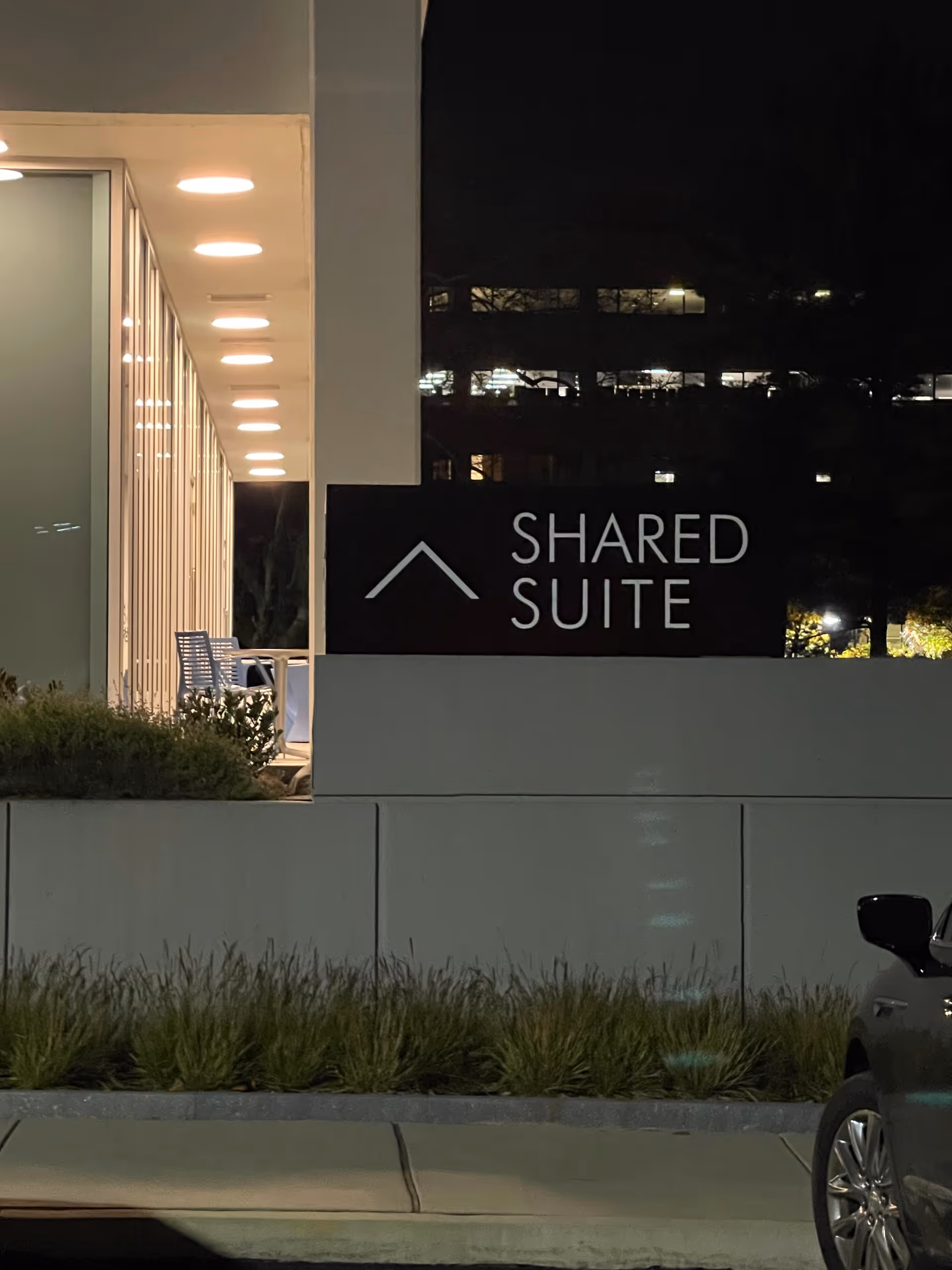 Night exterior of a building with a Shared Suite sign and outdoor seating.