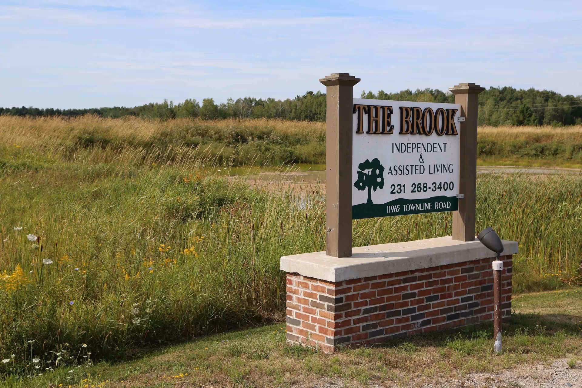 Outdoor sign for The Brook independent and assisted living, mounted on brick pedestal in a field.