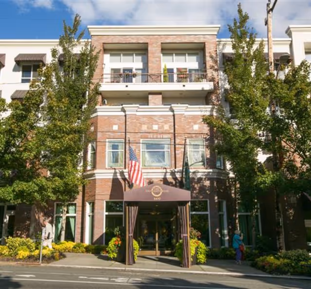 Brick senior living facility front entrance with flags, awning, and trees.