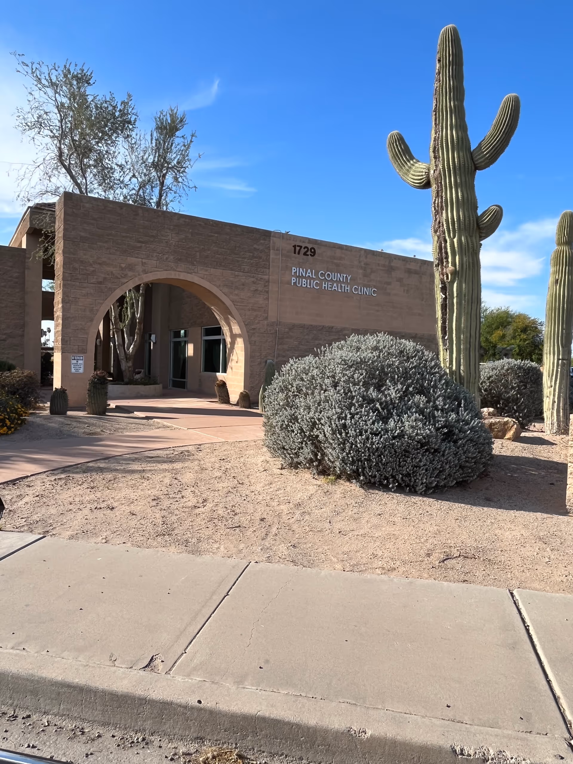 Exterior view of a brick clinic with an arched entrance and tall cacti.