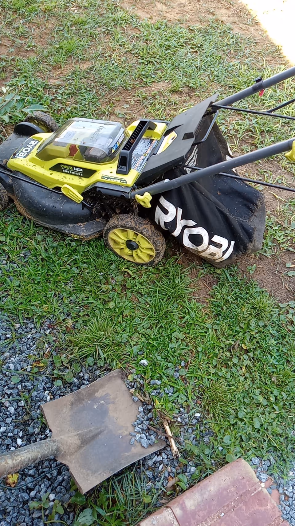 Lawn mower and gardening tools rest on a grassy outdoor area.