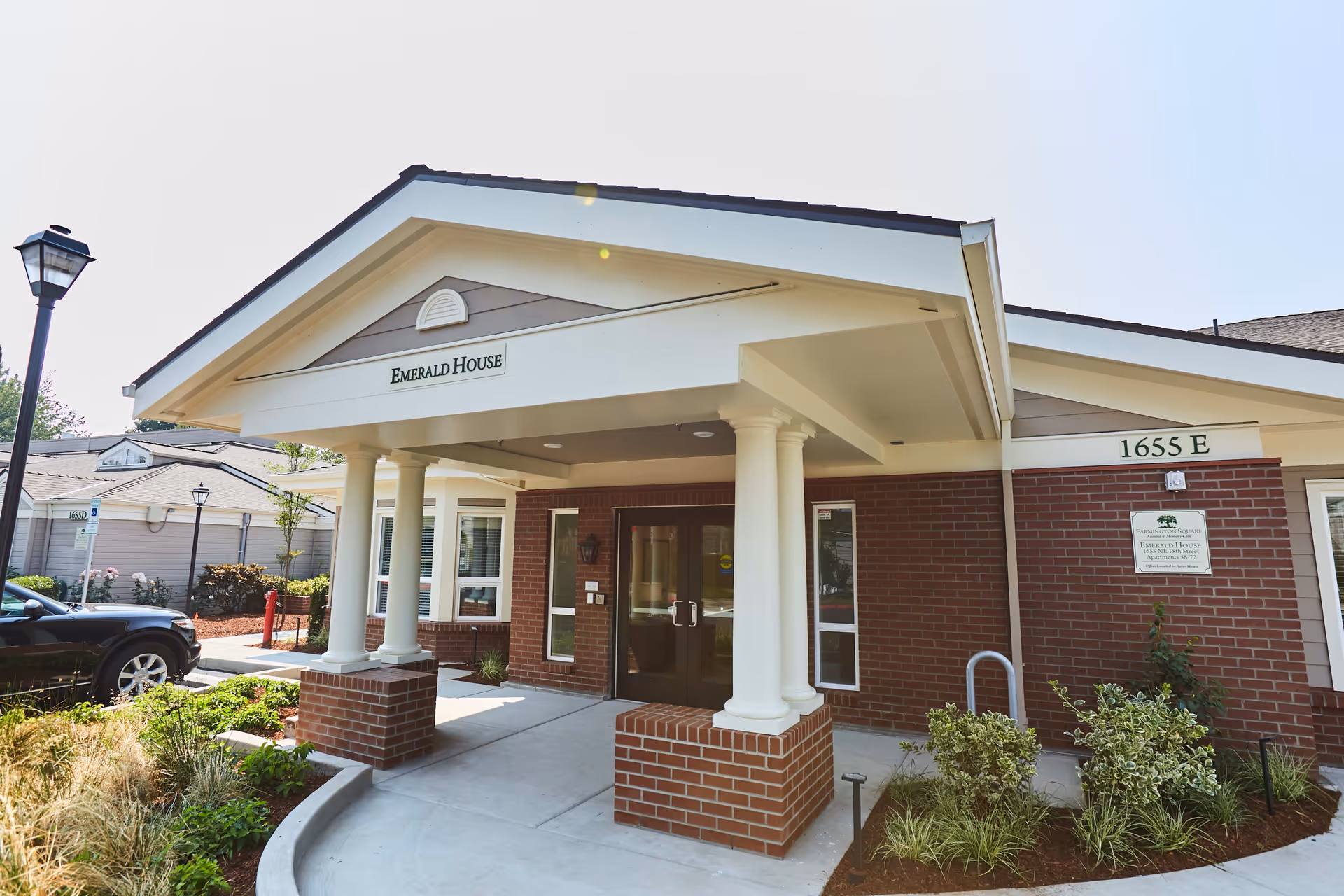 Front entrance of a single-story senior living building labeled "Emerald House" with white columns and a brick facade at 1655 E.