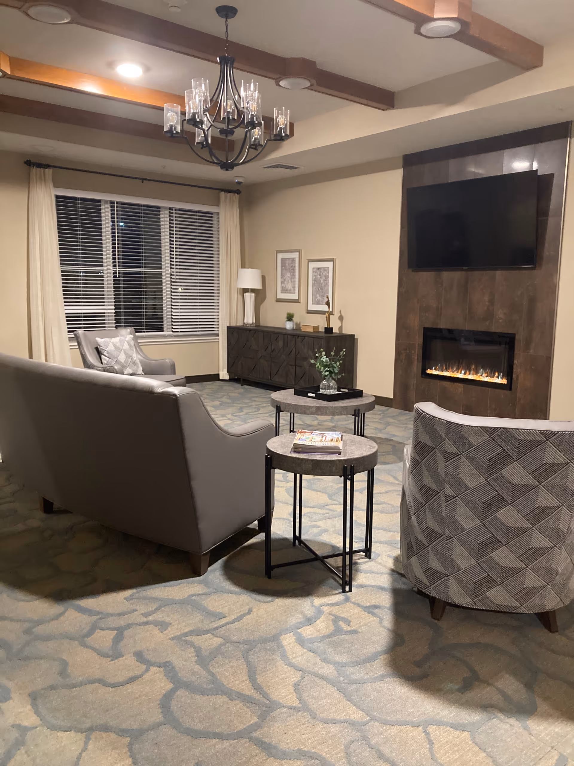 Cozy lounge in a senior living lobby with a fireplace, chandelier, and seating.