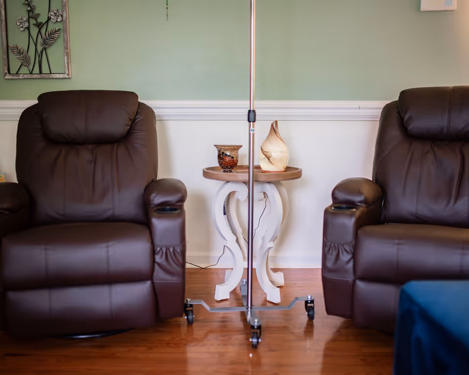 Two brown leather recliners flank a decorative table with an IV pole between them.