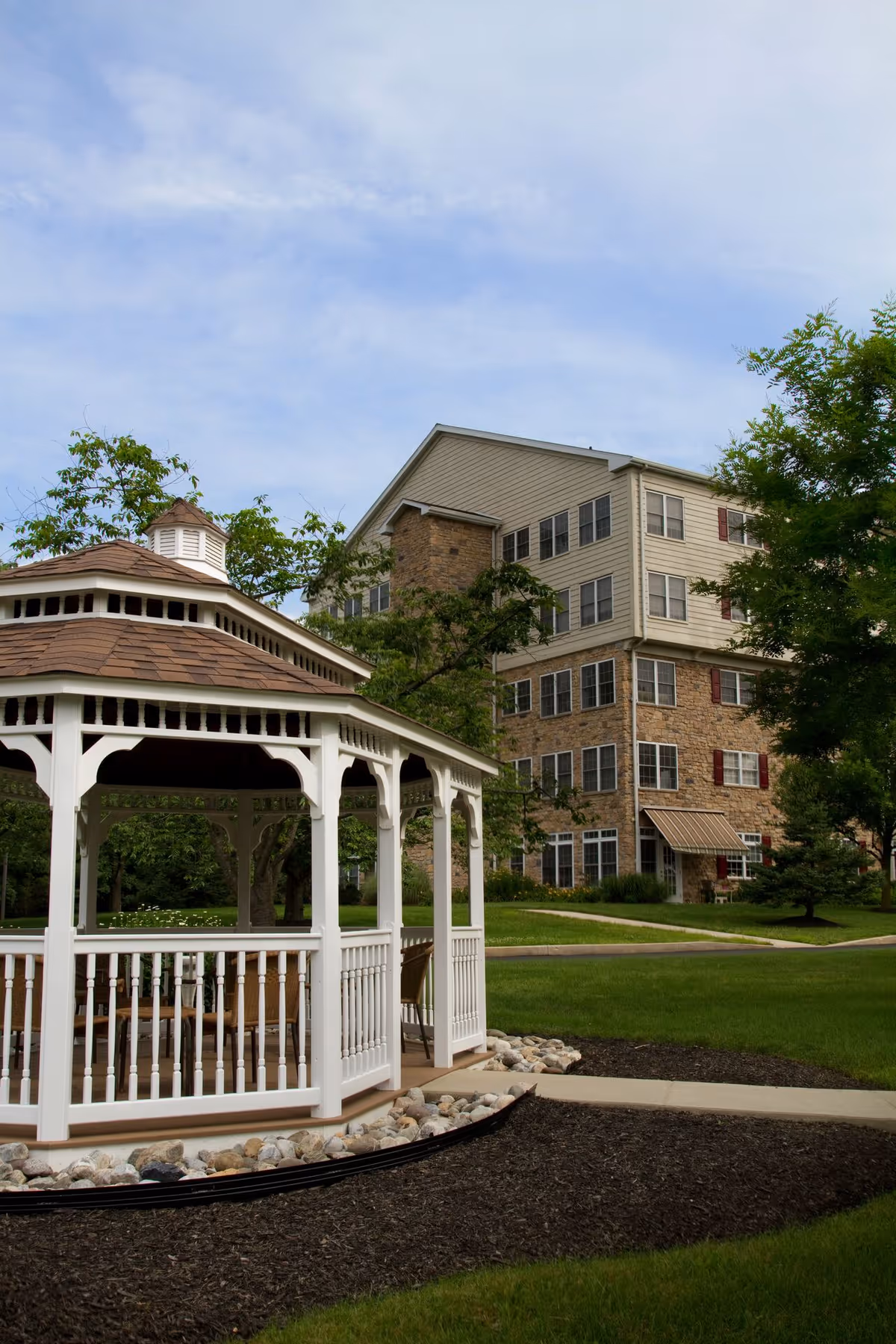White wooden gazebo on a lawn in front of a multi-story residential building.
