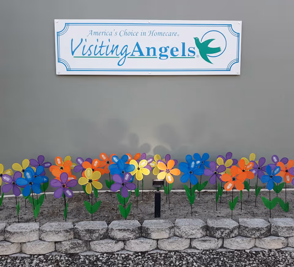 Colorful pinwheels line a stone border beneath a Visiting Angels sign.