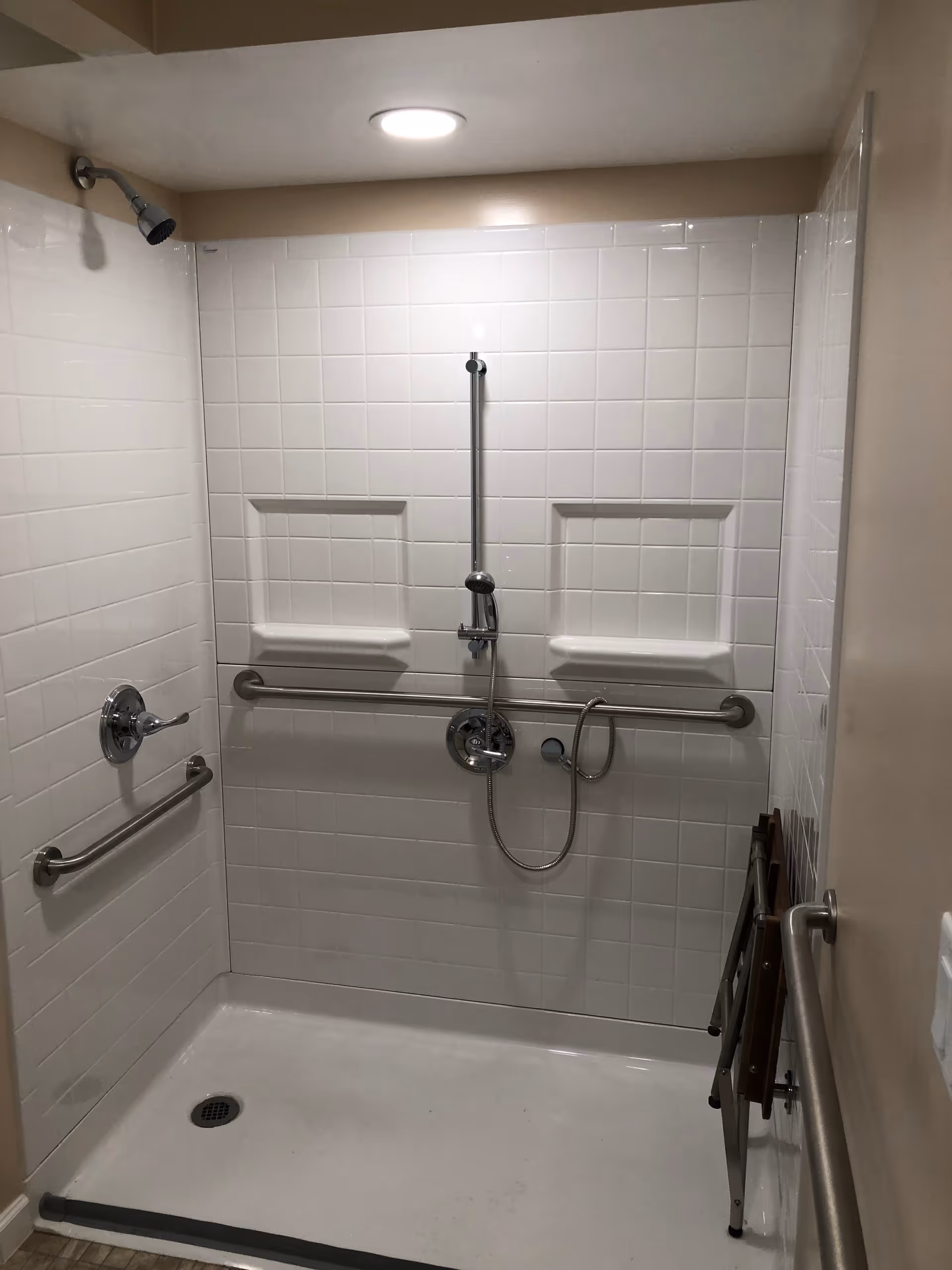 Accessible tiled shower with grab bars, a handheld shower, and built-in niches.