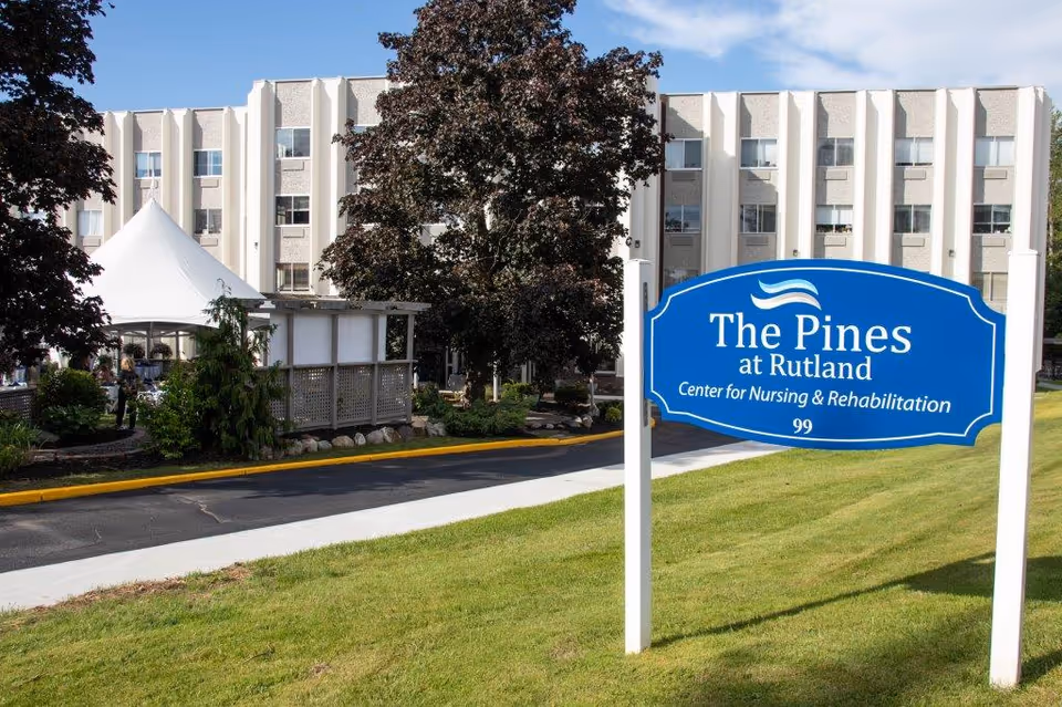 Blue sign reading The Pines at Rutland stands by the exterior nursing facility.