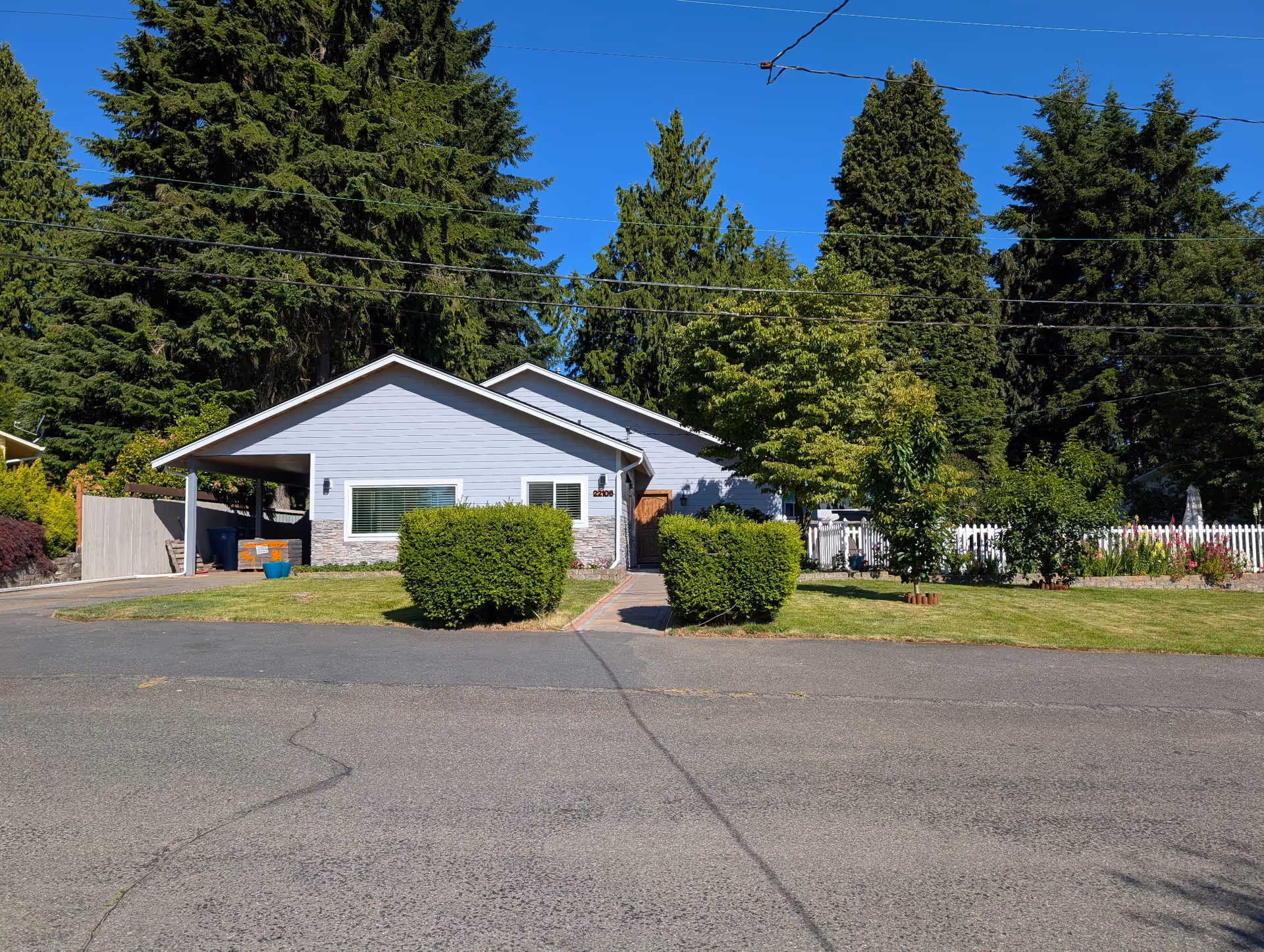 Single-story light-blue Affordable Luxury Care AFH house with carport and trimmed hedges.