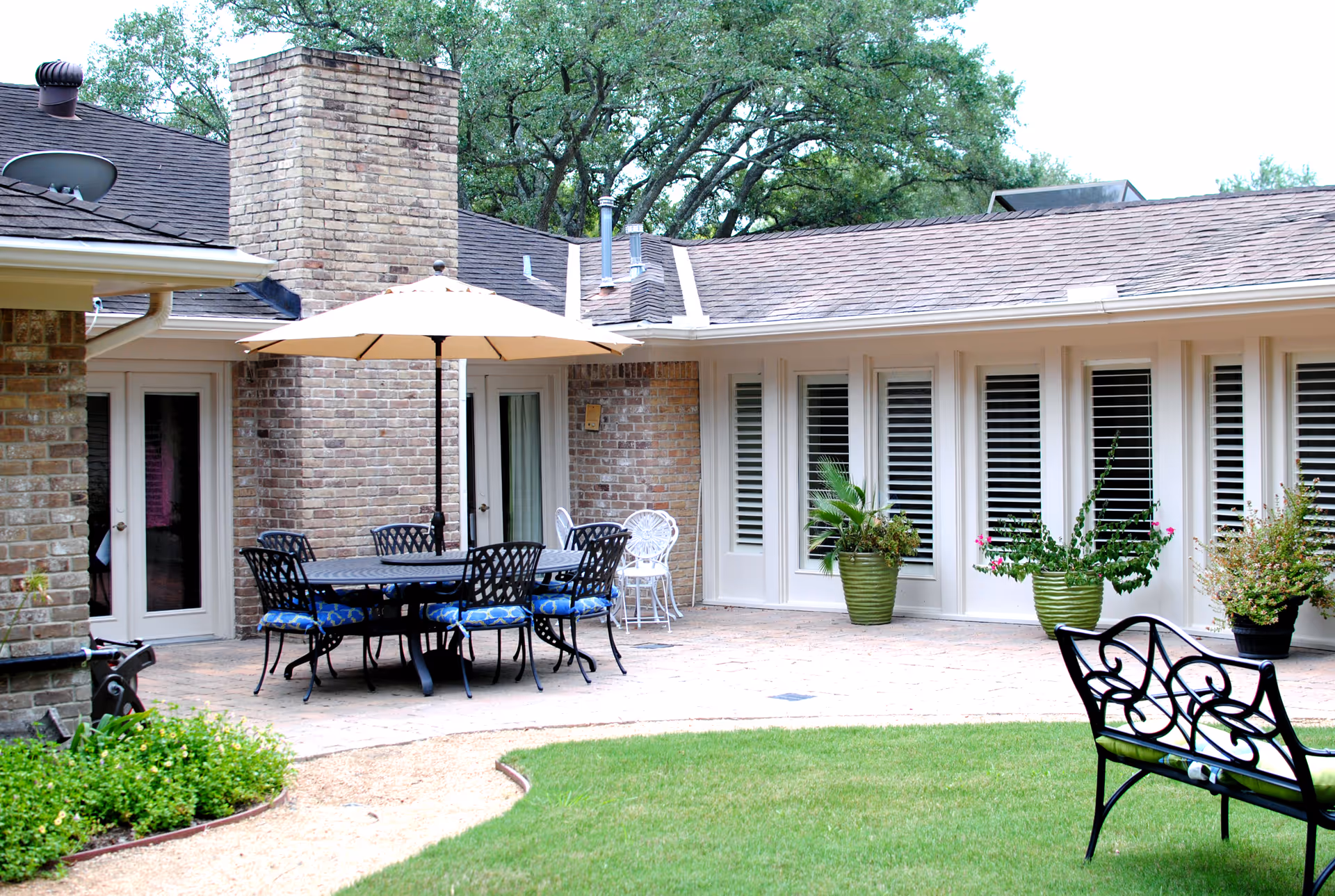 Outdoor courtyard of Autumn Years II Assisted Living Facility with a large table, umbrella, and chairs.
