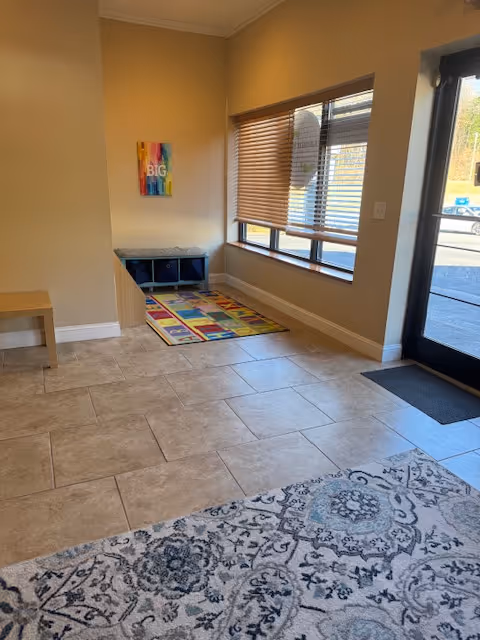 Entrance lobby with tiled floor, colorful rug, cubbies, window blinds, and a doorway.