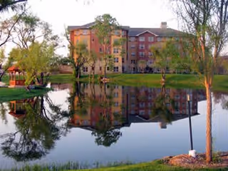 A multi-story Highland Springs senior living building sits by a calm lake with trees.