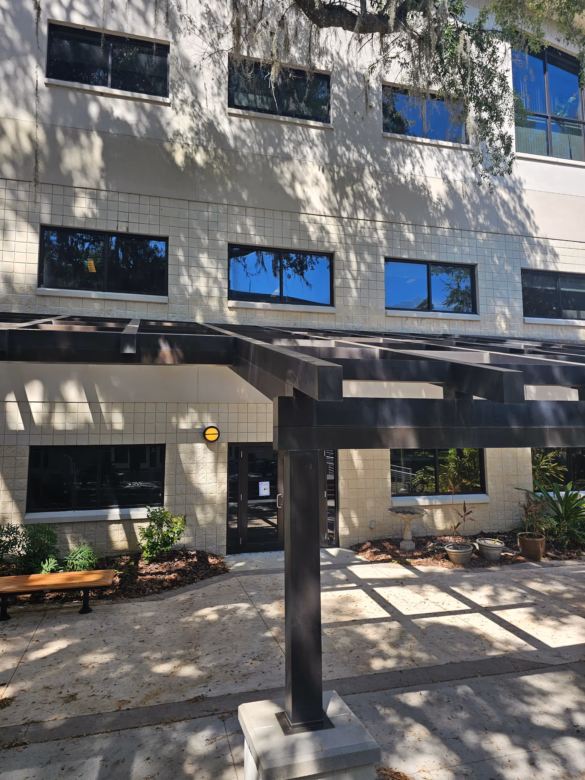 Senior living facility building exterior with windows, entrance, pergola, and potted plants.