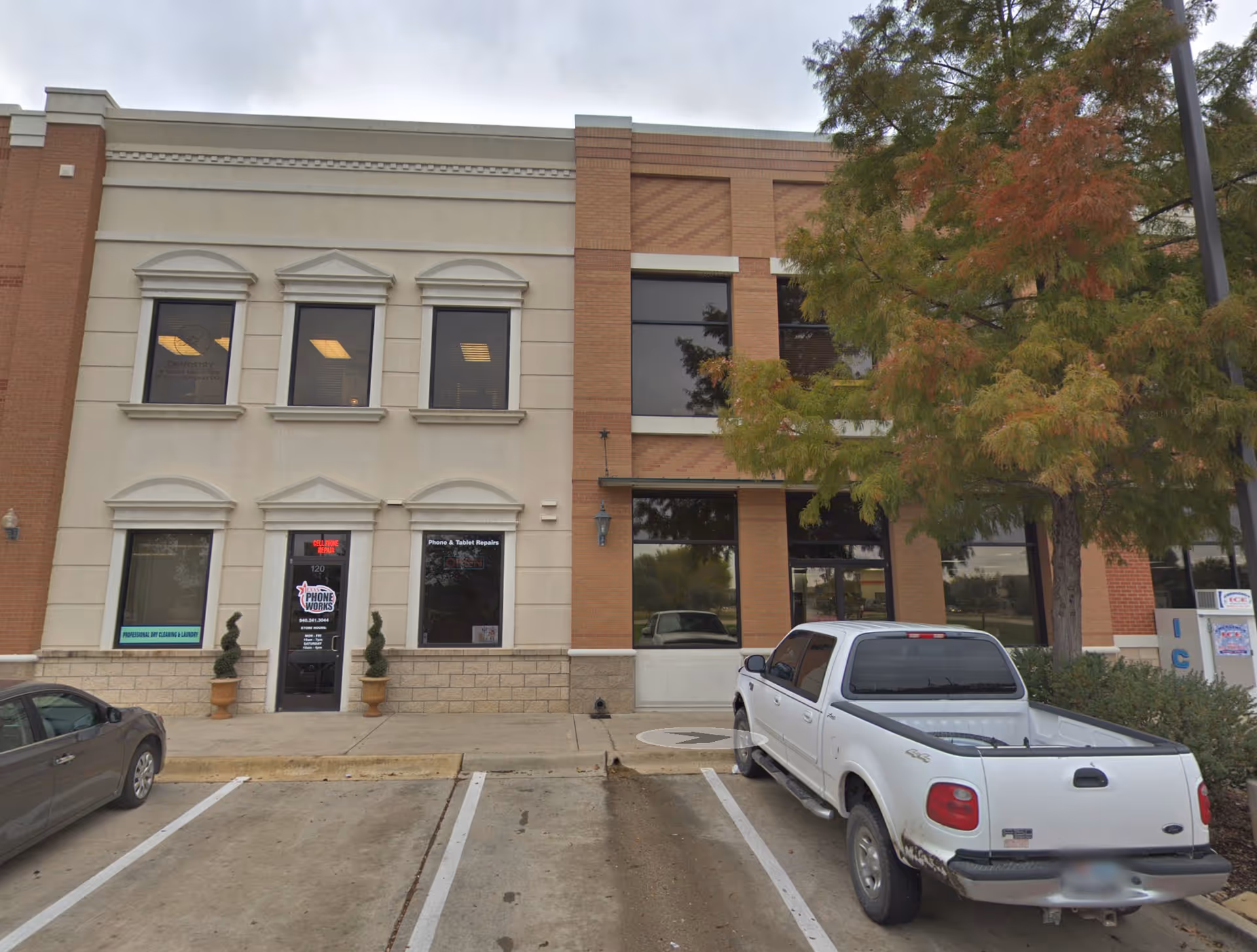 Two-story commercial building with brick detailing, large windows, and a white pickup in a parking lot.