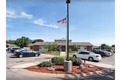 Prairie Villa senior living facility exterior with flagpole, parking lot, and landscaped entrance.