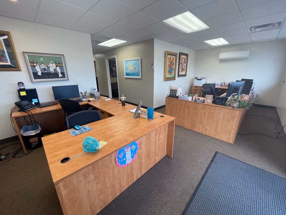 Interior office reception area with desks, computers, chairs, and framed artwork on walls.