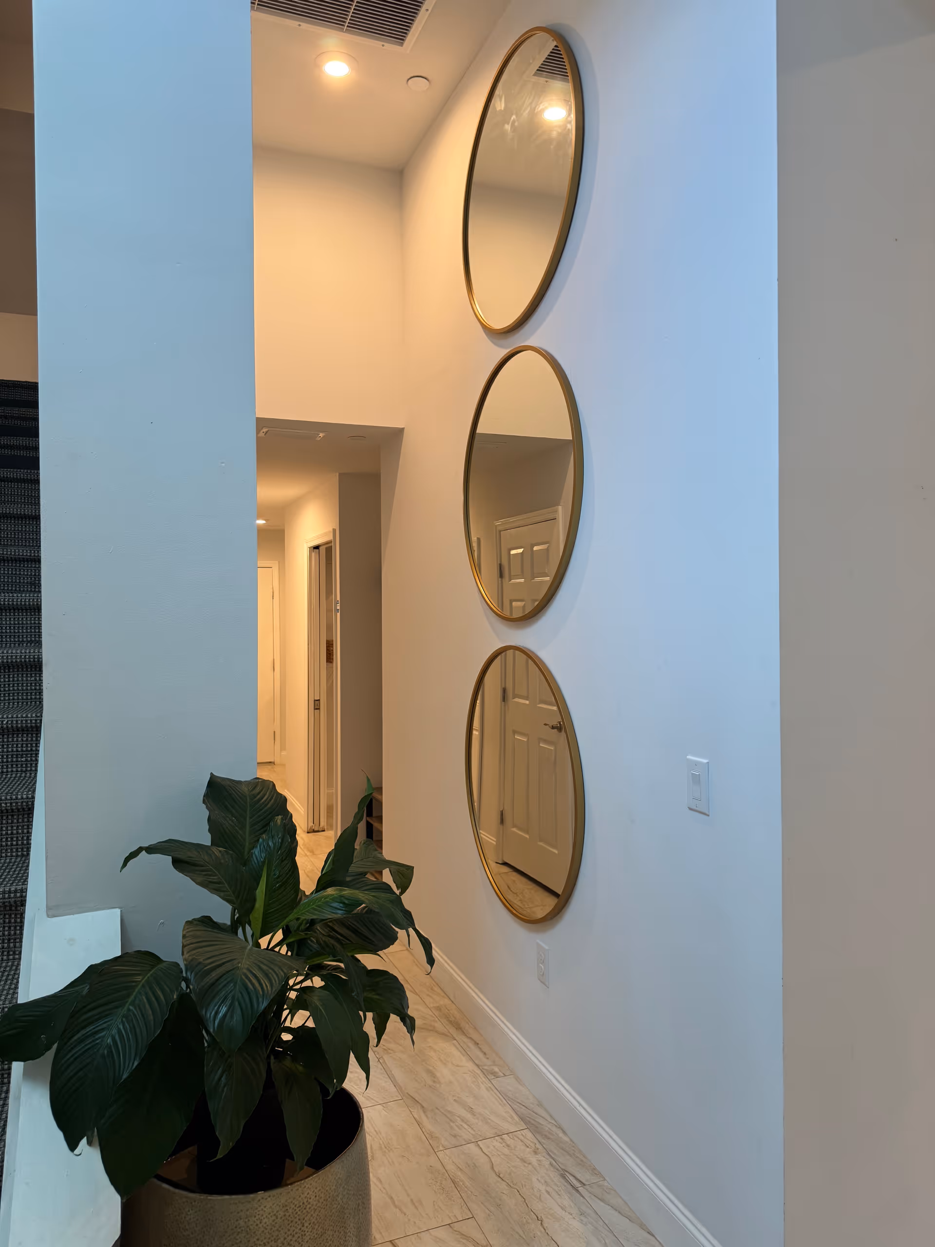 Tall hallway in a senior living facility with three round mirrors and a potted plant.