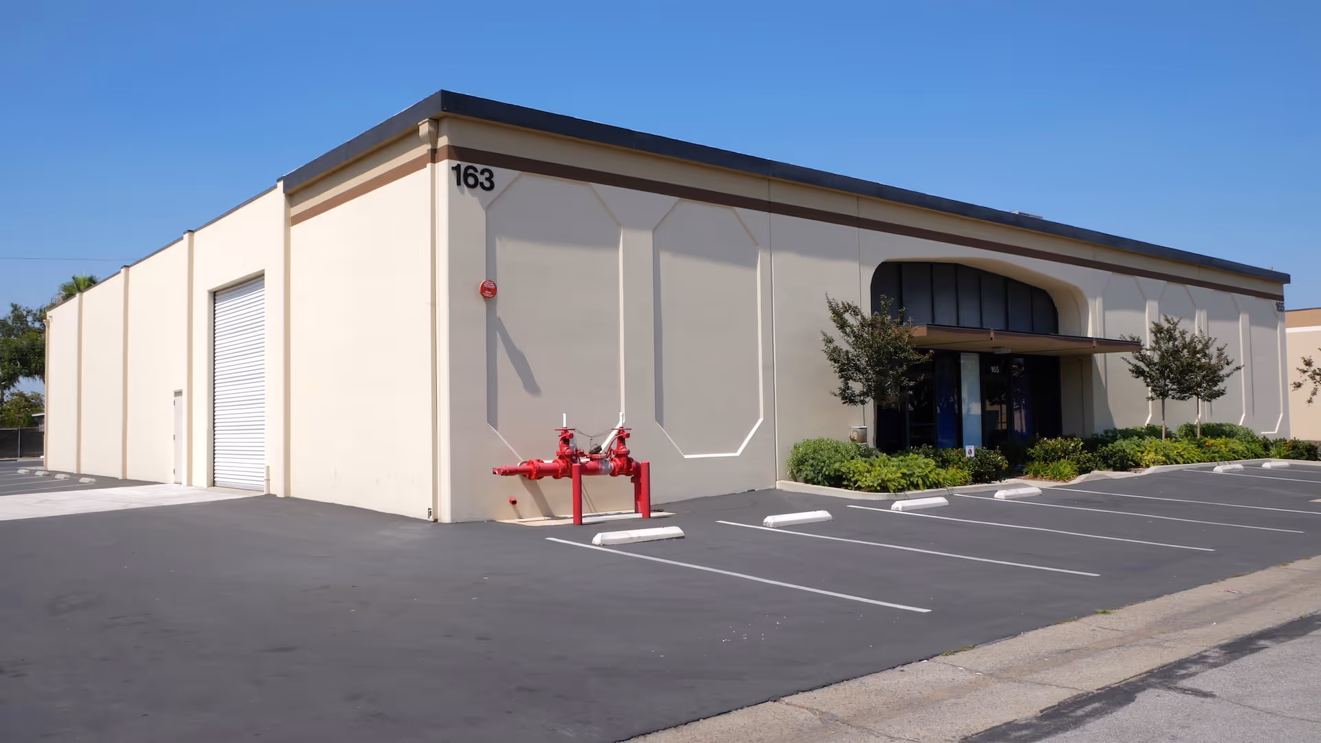 Beige rectangular building with arched entrance, parking lot, and red fire hydrant nearby.