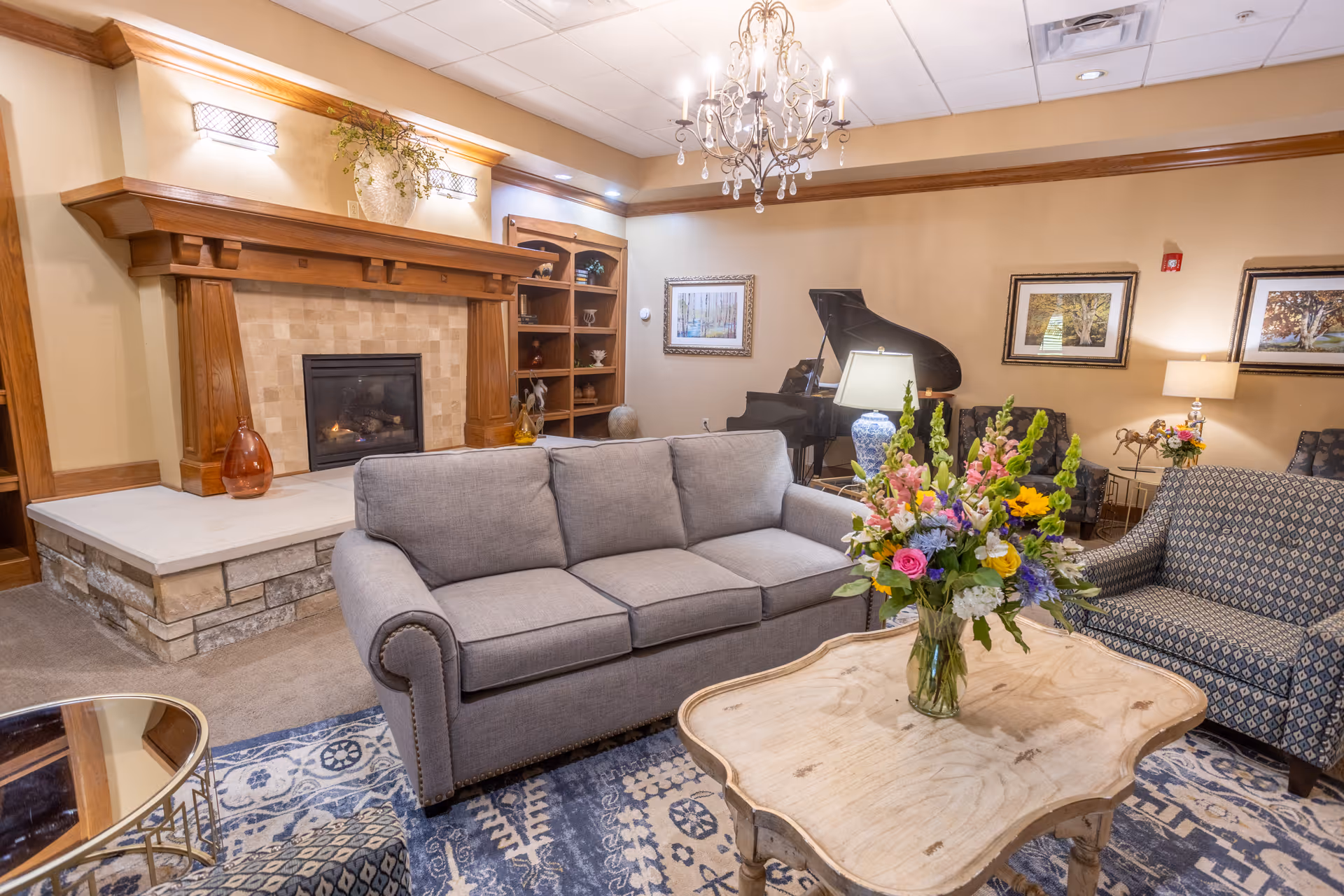 Cozy living room with fireplace, chandelier, sofa, piano, and floral centerpiece.