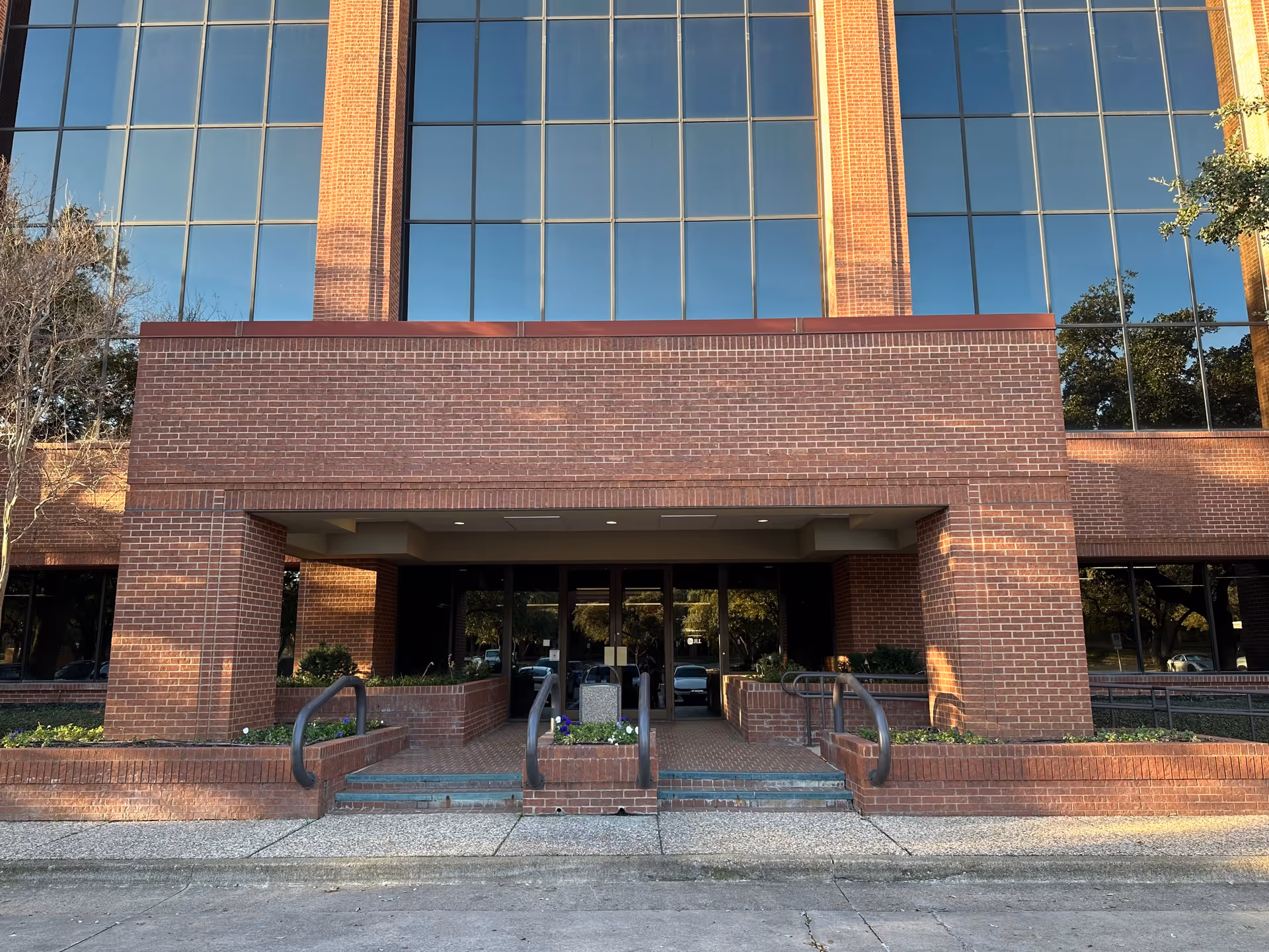 Brick building with large glass windows and a recessed entrance with steps and ramps.