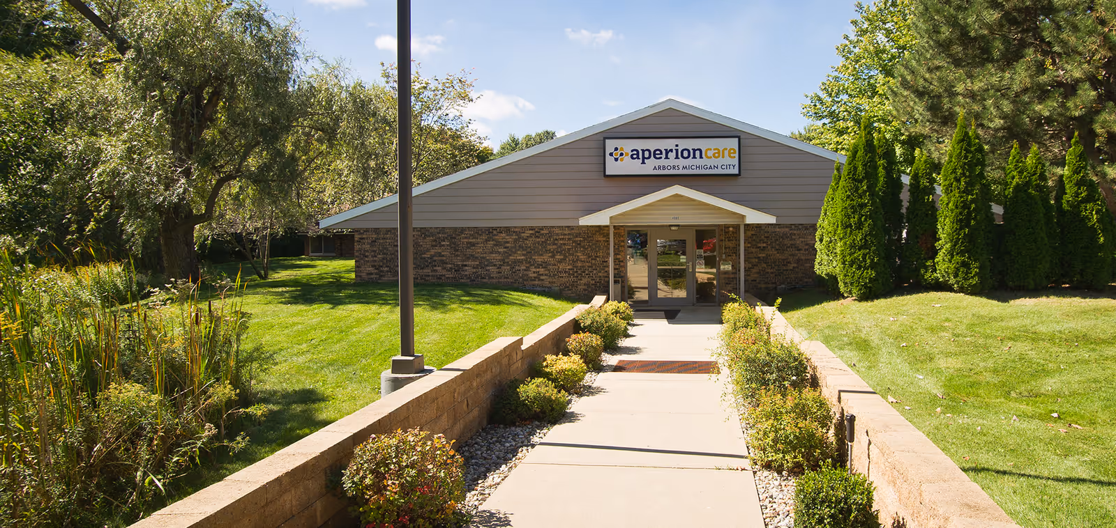 Pathway and landscaped grounds leading to the front entrance of the Aperion Care Arbors Michigan City building.