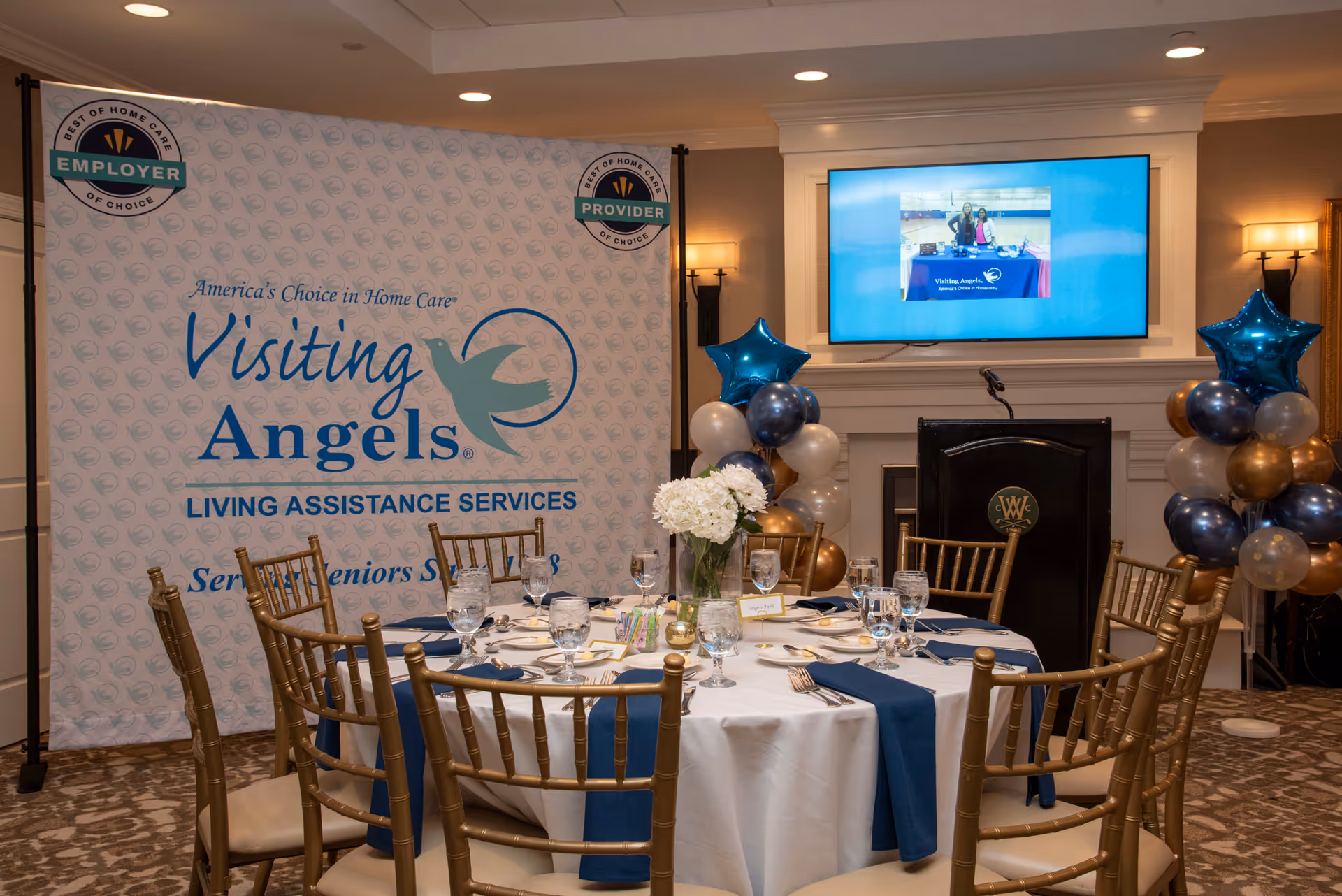 Round banquet table set for an event in a decorated room with Visiting Angels banner.