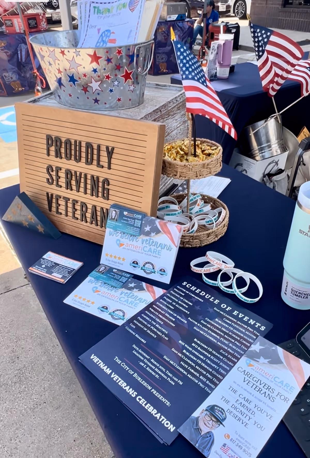 Outdoor table displays veterans event materials with American flags and brochures.