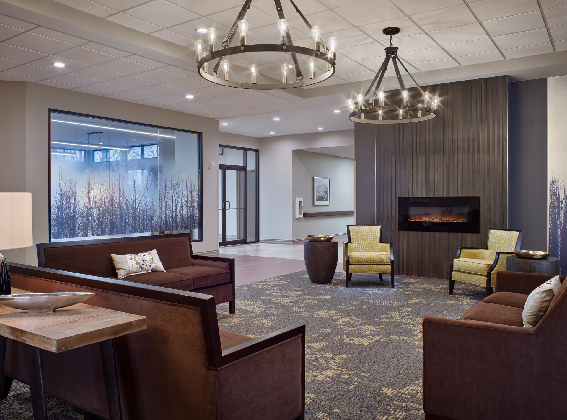 Spacious senior living lounge with sofas, chairs, fireplace, and chandelier lighting