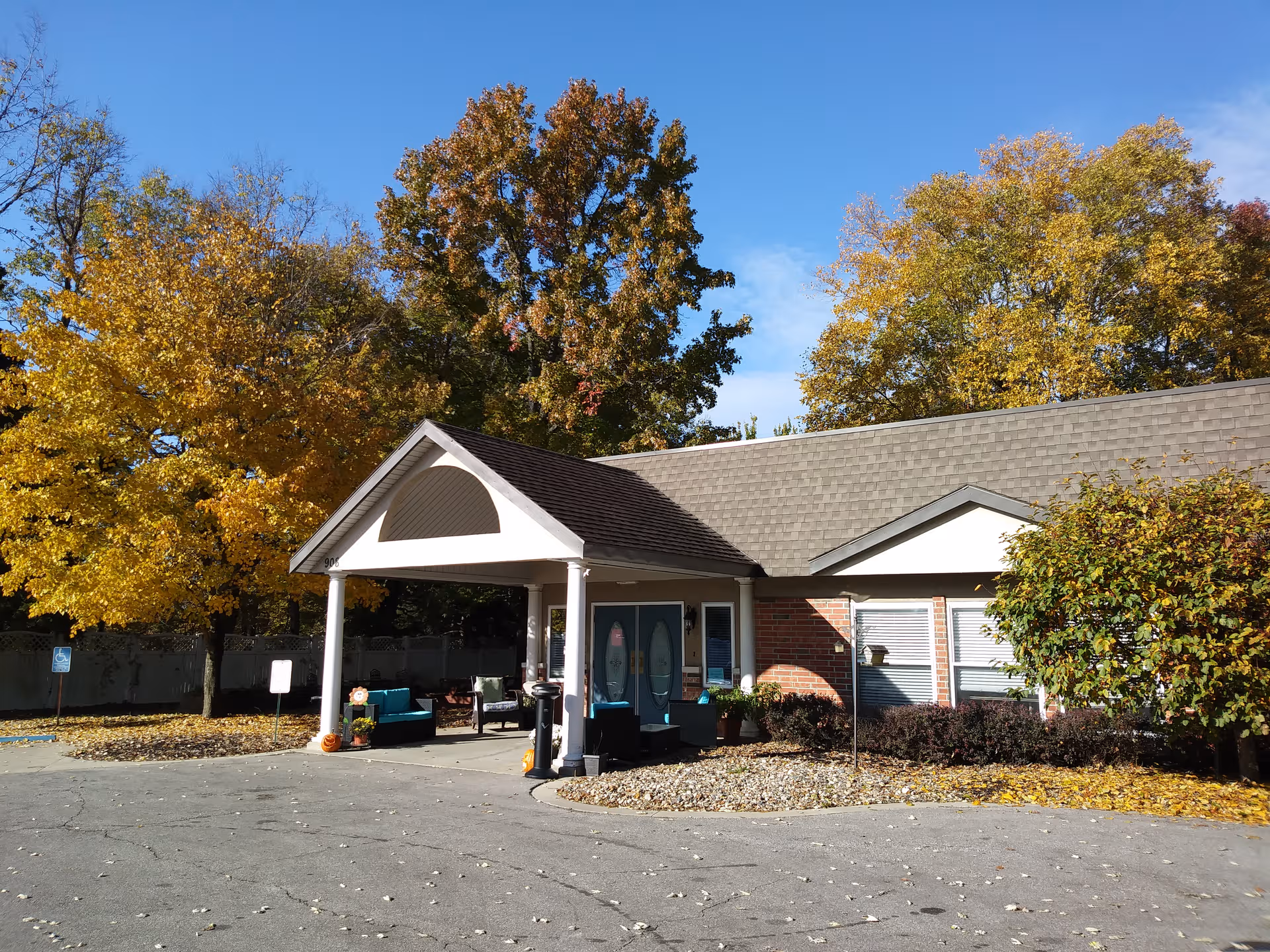 Senior living facility exterior with covered entrance and autumn trees framing the front