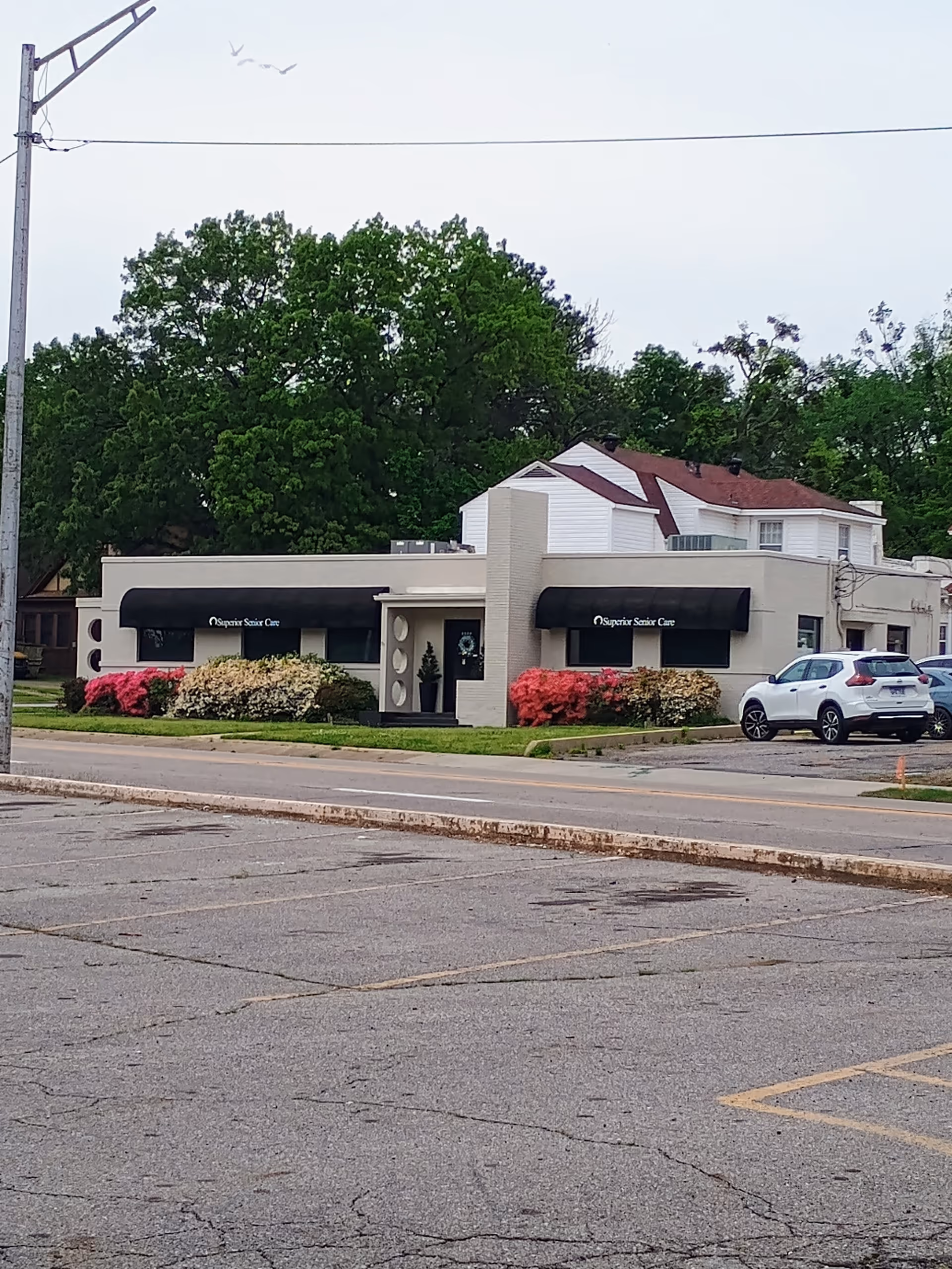 A single-story Superior Senior Care building with black awnings, landscaped bushes, and a parked car.