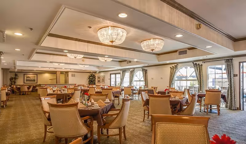 Large, well-lit dining room with multiple tables set for meals and crystal chandeliers.